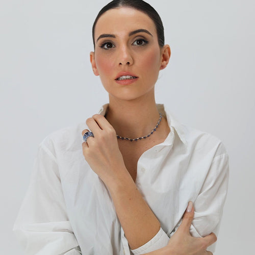 Realizado en plata de primera ley 925 milésimas y acabado con un baño de rodio blanco, se compone de una piedra principal en zafiro azul, talla cuadrada de 6 milímetros. Los hombros están engastados con infinitas piedras en talla gota y talla marquesa en distintas tonalidades de azul, desde el azul agua marina hasta el azul zafiro, pasando por el azul topacio.