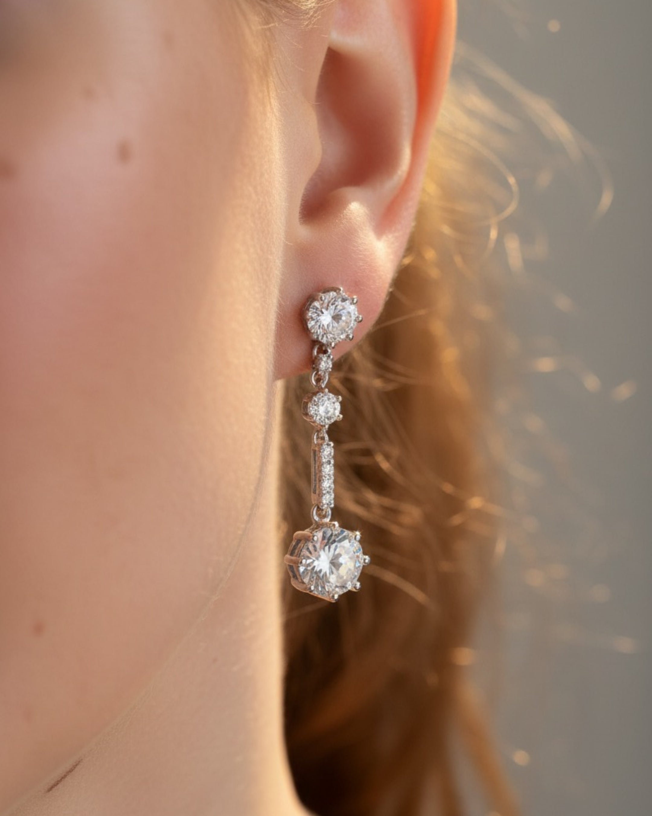 Detalle de los pendientes CORA con piedras blancas en talla circular que reflejan la luz con intensidad.