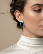 Pendientes elegantes con piedra azul central en talla gota rodeada de pequeñas piedras luminosas.