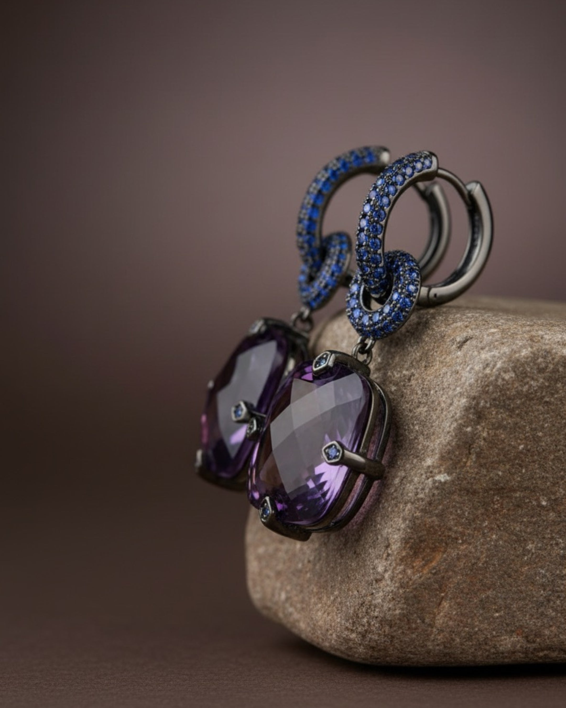 Pendientes Lyss con piedra principal en talla radiant violeta, montados en base de alta calidad Sibela con chapado en rodio negro. Una joya impactante y sofisticada.