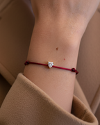 Pulsera de hilo rojo para mujer con acabado dorado y piedra brillante.