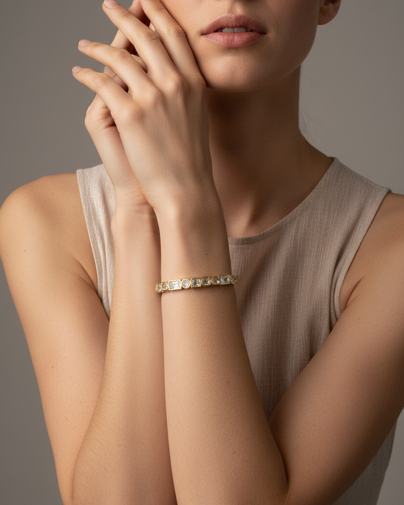 Pulsera KAIR dorada puesta en la muñeca, diseño rígido ajustable con piedras blancas y acabado en oro de 18 kt.
