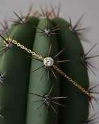 Pulsera minimalista con piedra blanca central y acabado en oro amarillo, diseño versátil.