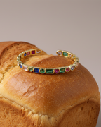 Pulsera rígida TALA con piedras de colores y estructura abierta ajustable con acabado dorado.